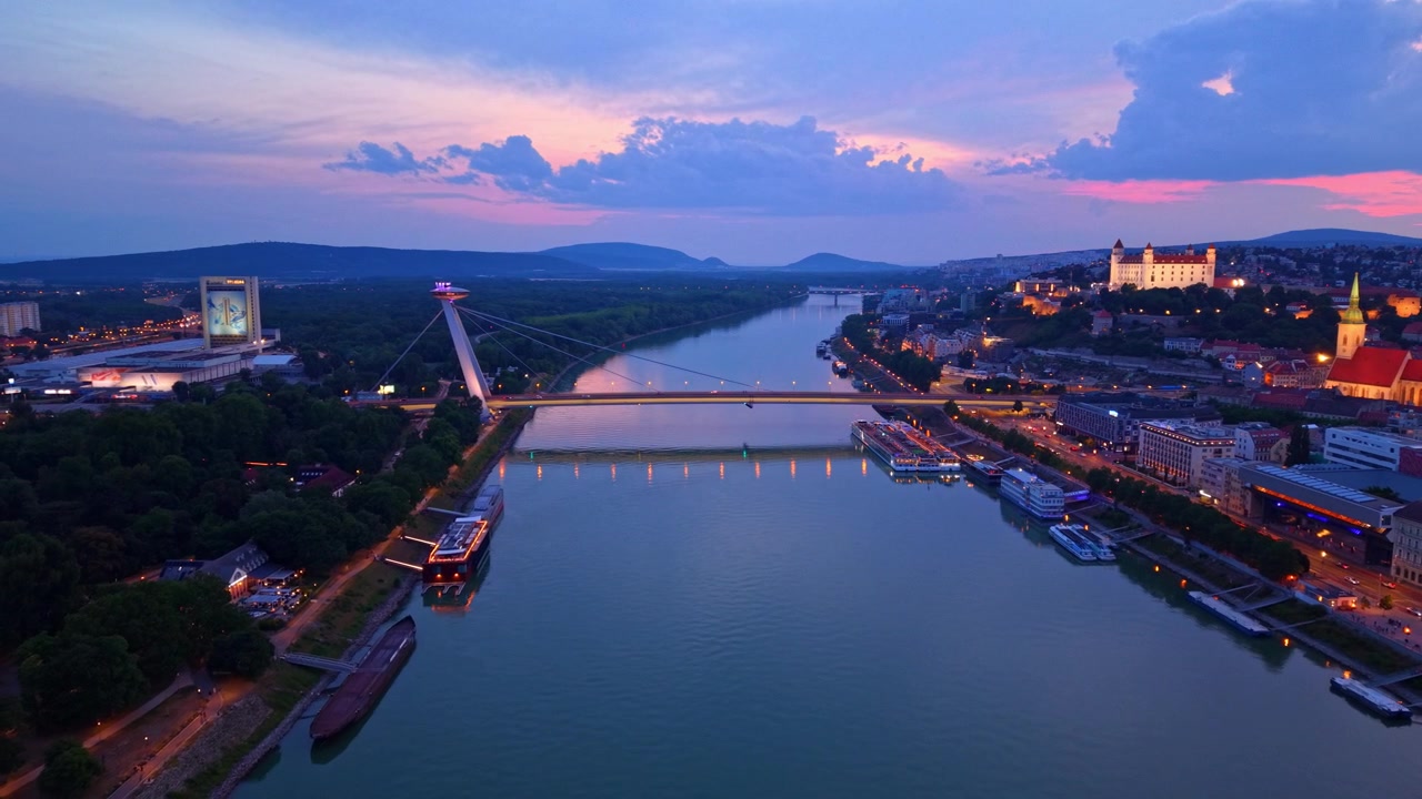 Donaufloden i Bratislava. Videoen viser Donaufloden, der strømmer gennem Bratislava under solnedgang, med broer og bygninger langs bredderne.