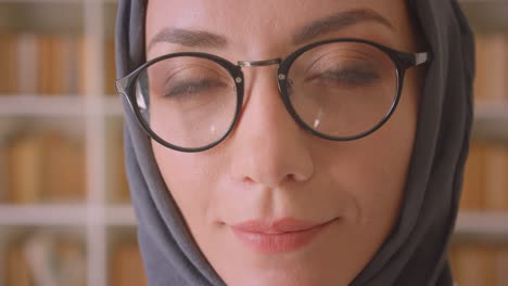 closeup portrait of young arabian female face in glasses and hijab looking at camera smiling cheerfully in library indoors