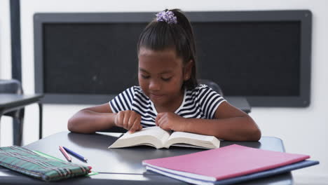 In-school,-in-a-classroom,-a-young-African-American-girl-is-focused-on-reading-a-book