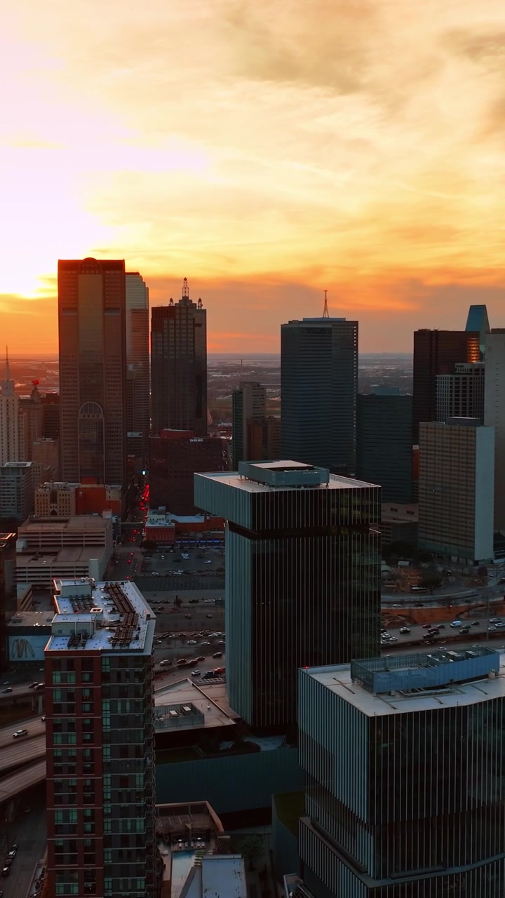 Tráfego intenso no centro de Dallas, Texas, EUA, ao pôr do sol. Belo céu laranja com nuvens claras ao fundo. Vista aérea. Vídeo vertical