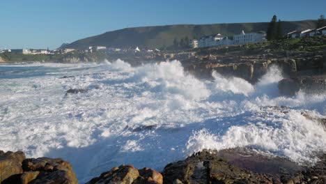 slow pan to right of wave crashing into rocks projecting water into sky, rough ocean