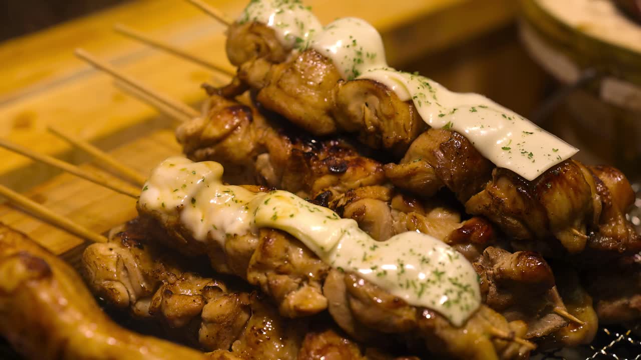 Close-up of skewered meat topped with melted cheese and herbs on a grill.