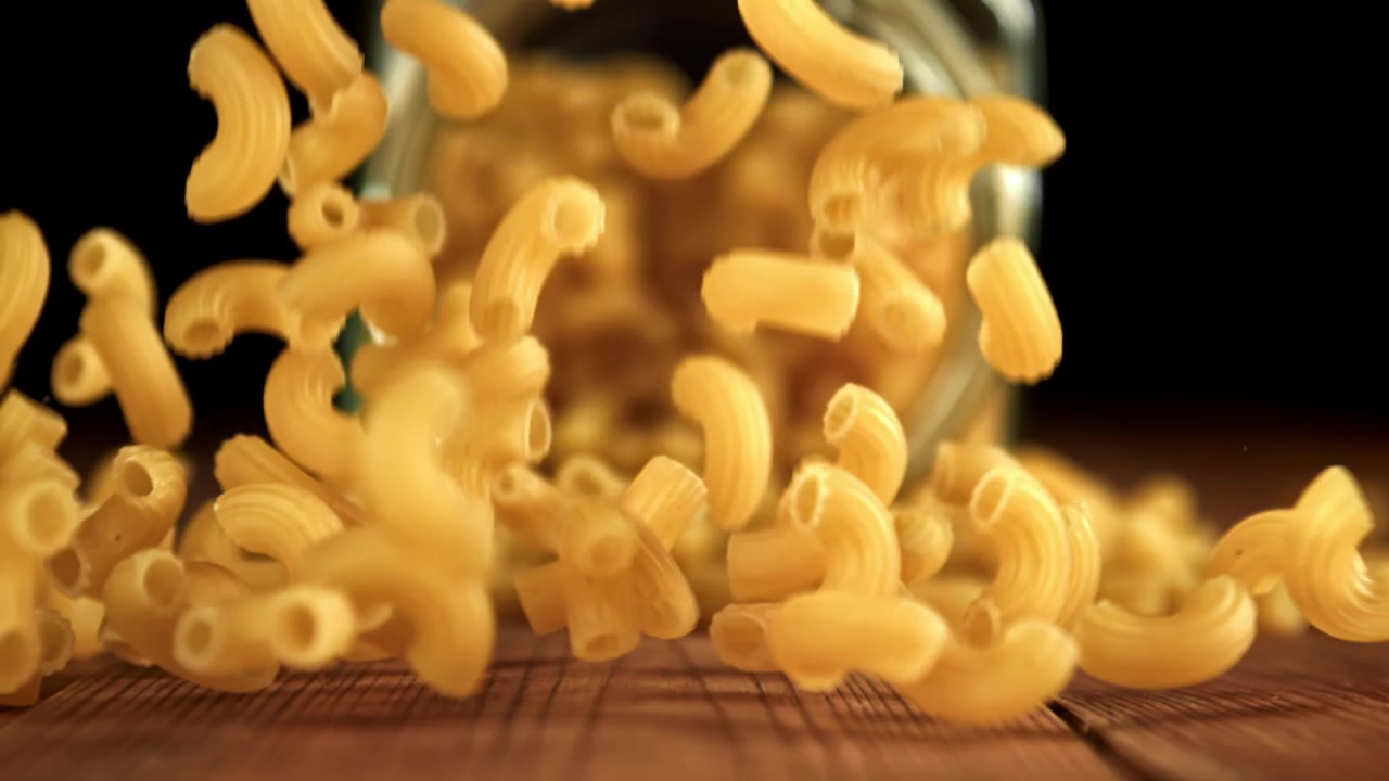 Maccheroni secchi che cadono da un barattolo su una superficie di legno