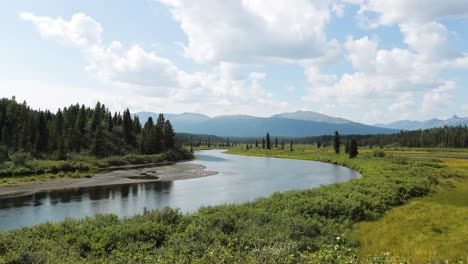 Time-Lapse-of-a-river-moving-with-a-bend-in-the-river-and-green-bushes-and-big-trees-and-mountains-in-the-background