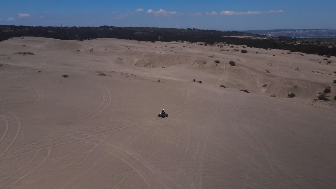 Aerial view following a motorcycle guy in the dunes of Ritoque on a sunny day