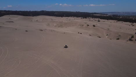 aerial view following a motorcycle guy in the dunes of ritoque on a sunny day