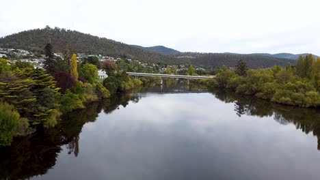 aerial - drone shot of bridge over beautiful river winding through a small town in tasmania