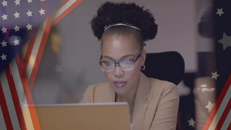 animation of flag of usa over happy african american businesswoman using laptop