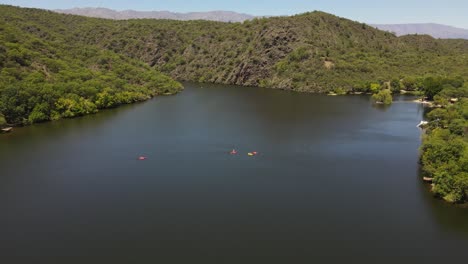 Toma-Aérea-De-Drones-Que-Muestra-A-Un-Grupo-De-Kayakistas-En-Medio-De-Un-Lago-Natural-En-Córdoba,-Argentina---Hermoso-Paisaje-Natural-Con-Montañas-En-Verano