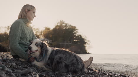 A-middle-aged-woman-sits-on-the-picturesque-shore-of-Lake-Ontario-with-her-dog-next-to-her.