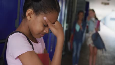video de una triste chica biracial burlada por dos chicas diversas en el pasillo de la escuela, espacio de copia