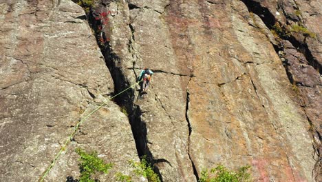 aerial footage tilting up past lone climber on cliff in maine