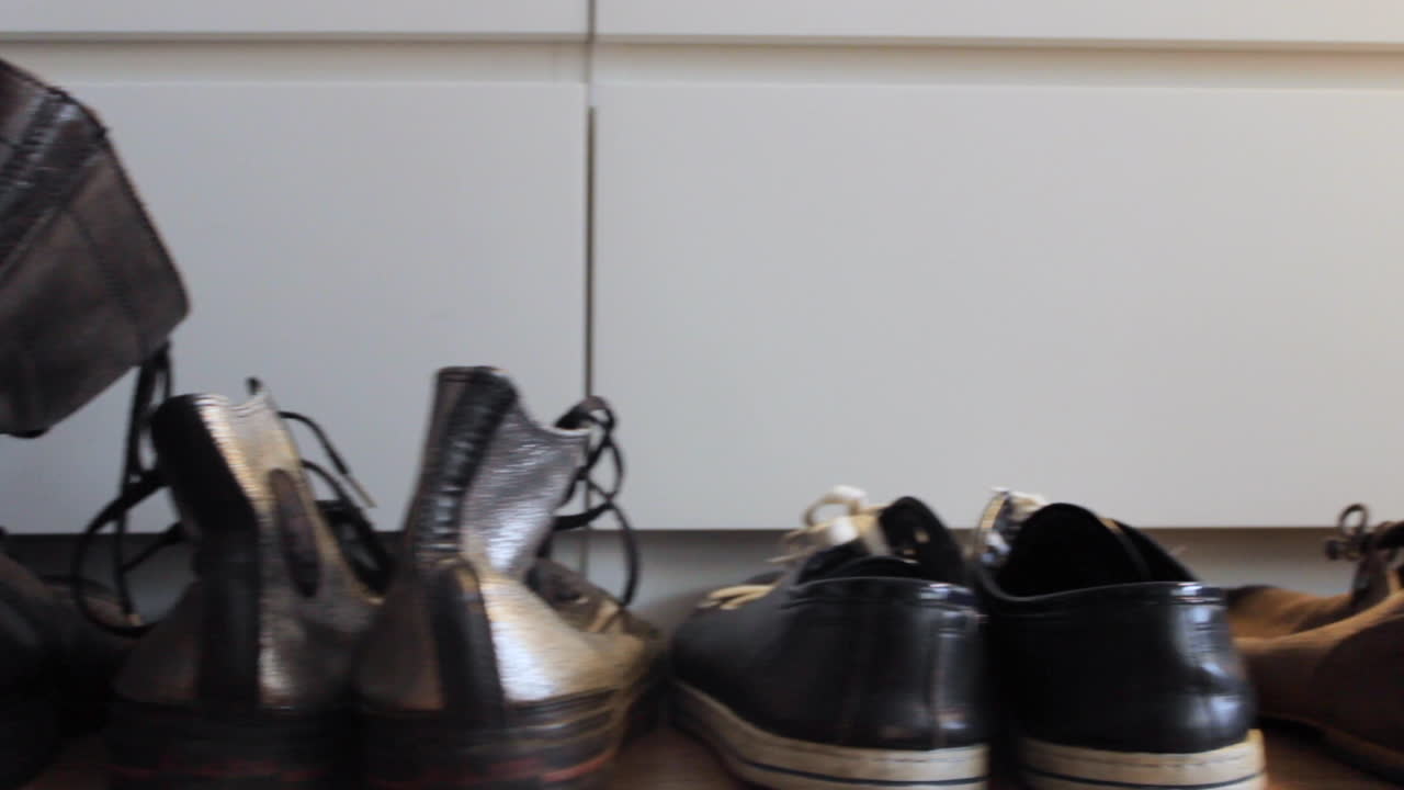 카메라가 신발 몇 켤레 옆으로 미끄러지고 백인 남자가 손으로 검은 신발 한 켤레를 집습니다.