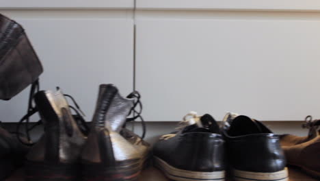 la cámara se desliza junto a unos pares de zapatos, y la mano de un hombre caucásico recoge un par de zapatos negros