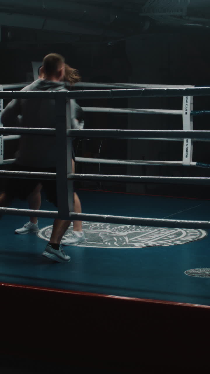 mujer atlética en guantes de boxeo se prepara para la lucha, la competencia y los ejercicios con el entrenador masculino en el gimnasio oscuro. boxeadora golpea guantes de puñetazos en el ring de boxe o tiro vertical