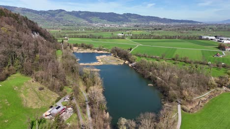 Oberriet-in-switzerland-with-a-meandering-river,-lush-fields,-and-distant-hills,-under-a-clear-sky,-aerial-view