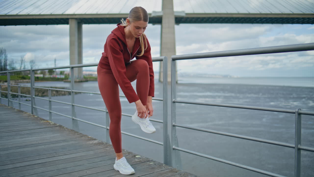 Fitness girl tying shoes at city bay. Urban runner preparing for cardio workout