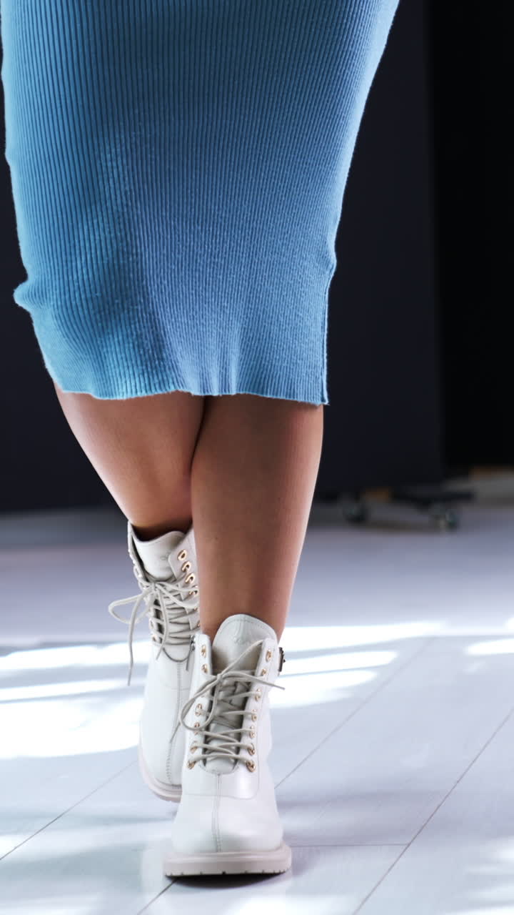 Female in blue midi dress walks by the room. Model demonstrating the boots made of leather, with tractor soles and laces. Vertical video