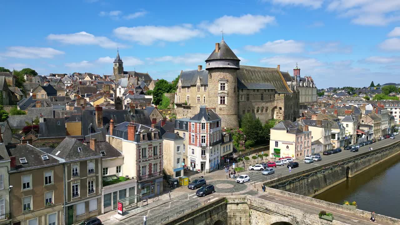 Lateral drone shot of riverside roundabout, partial bridge, buildings, light traffic, and old Laval Castle - France
