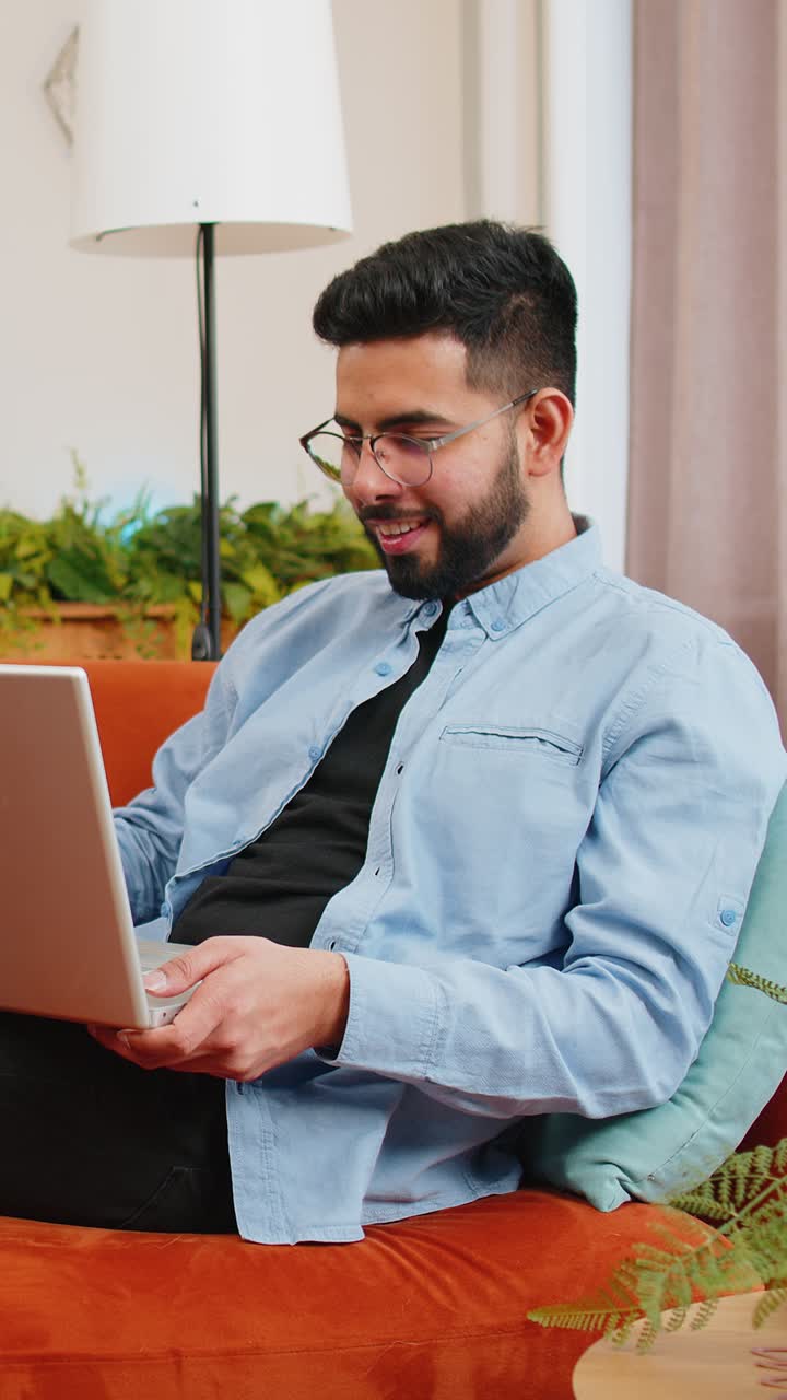 hombre indio escribiendo trabajando en una computadora portátil usando aplicaciones navegando por internet mintiendo estudiando educación en el sofá de casa