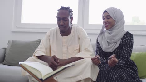 african muslim couple at home in ramadan reading quran holly islam book in modern apartment on sofa