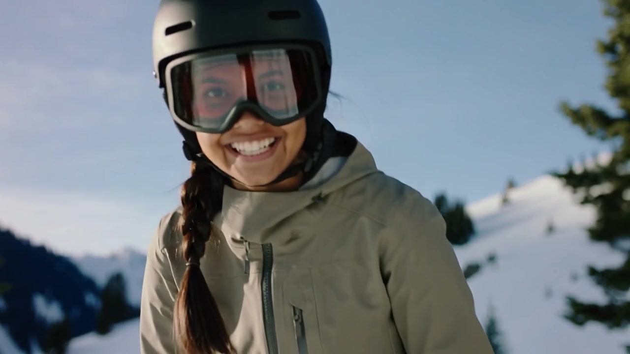 Snowboarder con casco che inserisce i piedi negli attacchi, preparandosi alla discesa su uno snowboard rosso, sorridente.