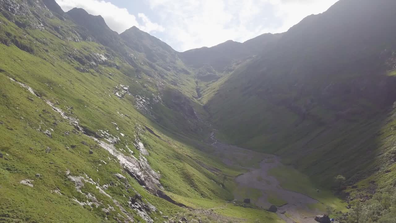 Verde e incontaminata Valle delle Tre Sorelle tra imponenti montagne a Glencoe, Scozia, in una giornata di sole parzialmente nuvolosa.