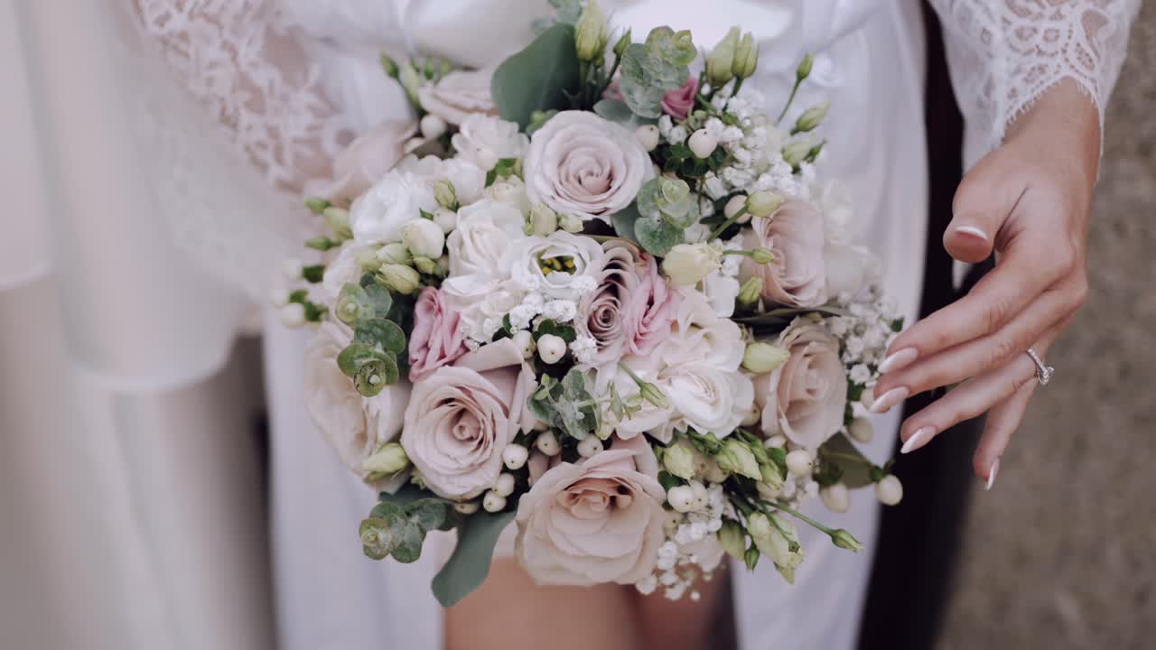 Primo piano di una sposa che tiene un delicato bouquet da sposa color pastello con fiori morbidi