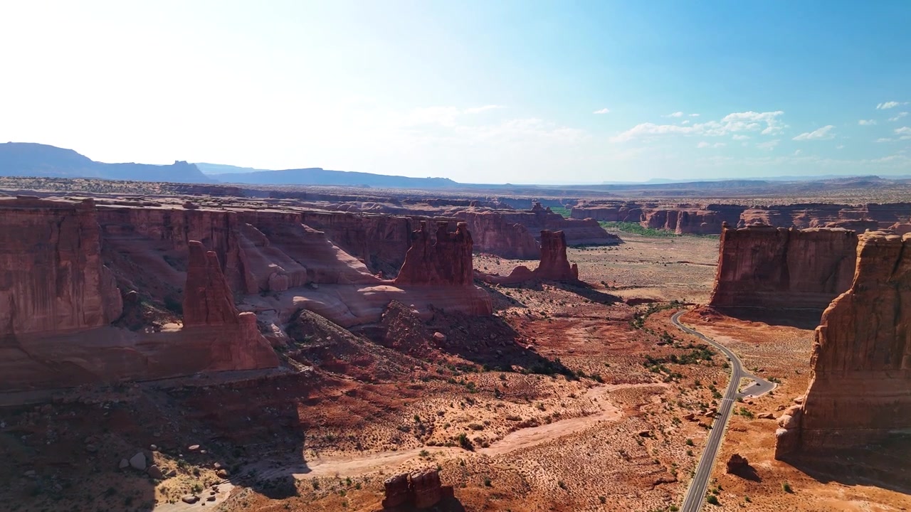 Splendido filmato stock del Parco Nazionale di Arches, USA, durante un pomeriggio luminoso. La luce solare brillante illumina le maestose strutture di arenaria rossa e il paesaggio desertico sotto un cielo azzurro limpido.
