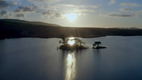 Aerial pullback backlit small island in Lough Bofin in the soft evening light, the setting sun casting a golden glow over the water, Connemara, Galway, Ireland