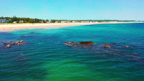 drone flies above saco, maine beaches packed with people. vacation homes line the busy sand as atlantic waves roll in. peak-season seashore scene shows vibrant travel life on the new england coast