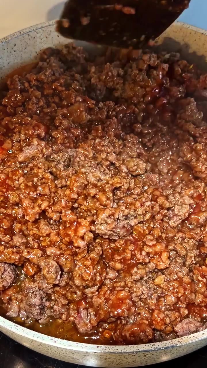 Carne macinata che sobbolle mescolandosi con salsa di pomodoro in padella durante la preparazione del pasto, verticale.