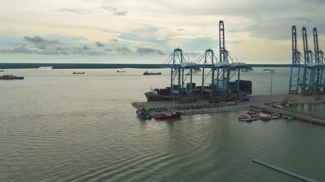 Container ship docked at Northport, Klang in Selangor, Malaysia during cargo loading. Industrial maritime scene with cranes, tugboats, and vessels under a cloudy tropical sky. UHD.