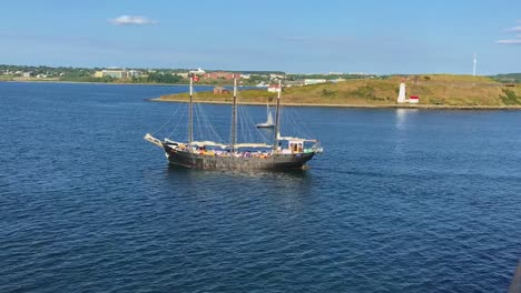 3-mast barque sailing vessel crusing in harbor in front of lighthouse on eastern coast of canada