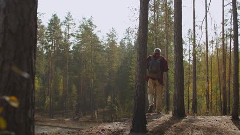 hiker-is-walking-alone-in-forest-at-autumn-sunny-day-fisherman-is-exploring-forest-with-lake-calm-entertainment-in-weekend