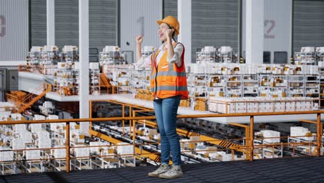 vista lateral completa del cuerpo de una ingeniera asiática con casco de seguridad de pie y gritando meta celebrando trabajando en el almacén con estantes llenos de mercancías de entrega