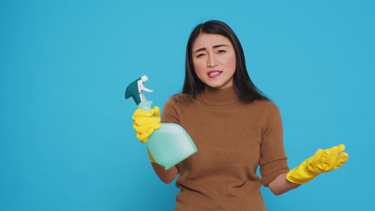 Upset house cleaner wearing yellow rubber gloves while showing chemical detergent spray