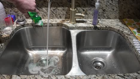 pouring green dish soap into the sink and making bubbles