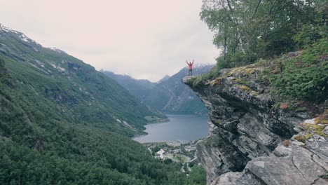 person standing on the edge of a mountain, throwing arms up into the air, surrounded by nature, mountains and watching over a beautiful lake