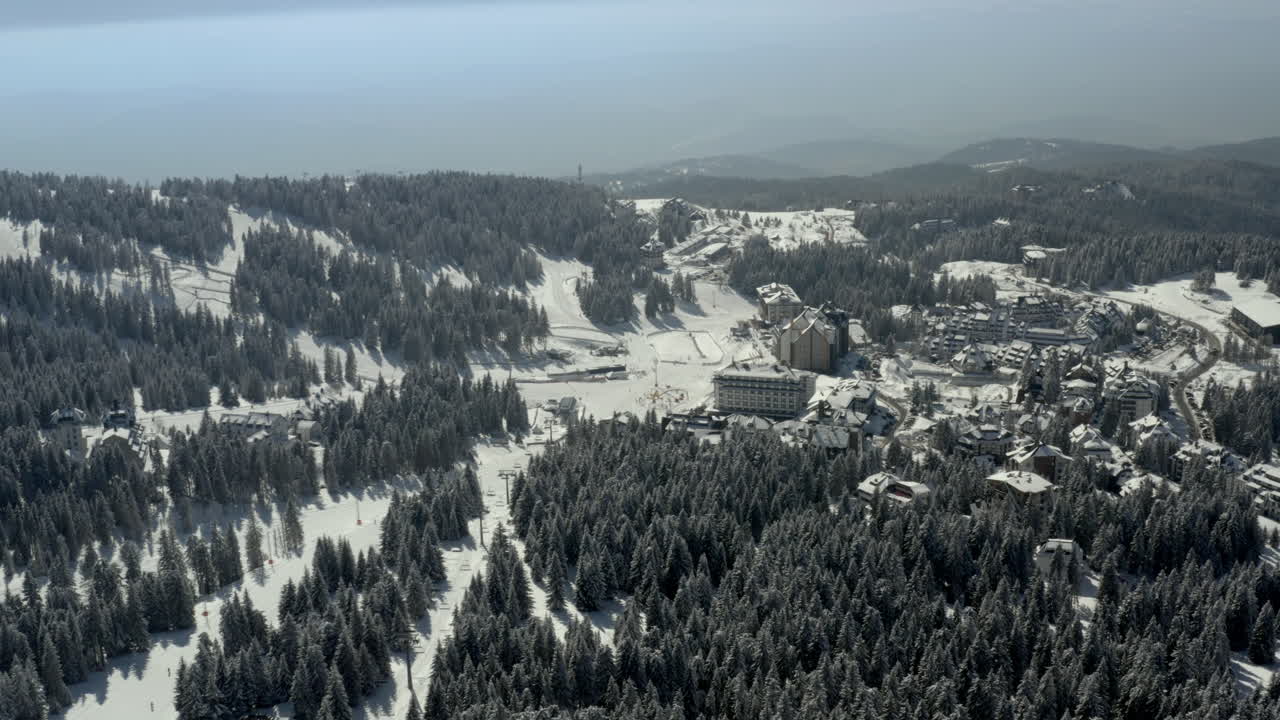 Aerial view of a snow-covered ski resort nestled in a dense pine forest on a mountain