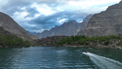 Vista-Aérea-De-La-Moto-Acuática-Cruzando-El-Lago-Skardu-Superior-De-Kachura-Con-Paisaje-De-Montaña-En-La-Distancia