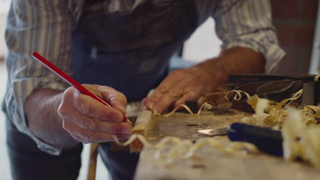 Mature-Male-Carpenter-In-Garage-Workshop-Measuring-And-Planing-Piece-Of-Wood