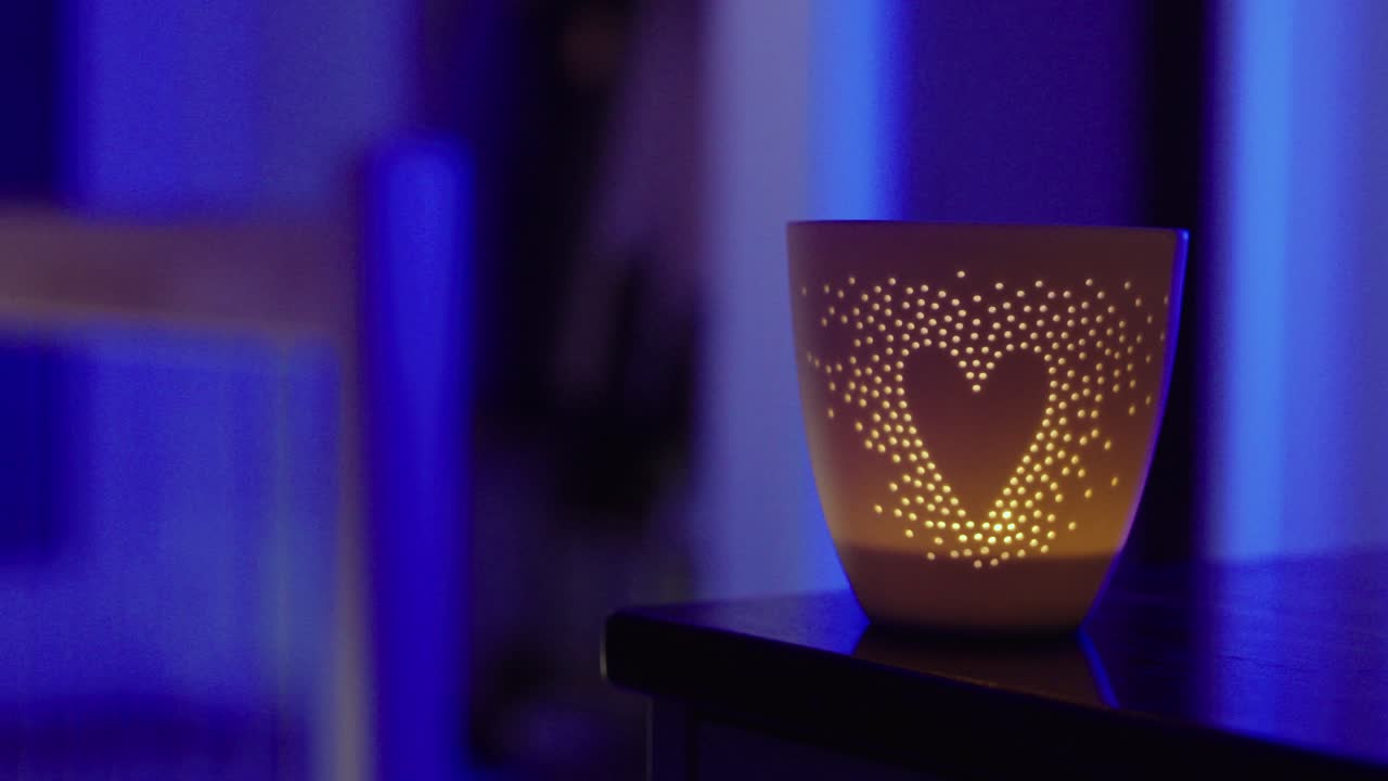 Gros plan cinématographique d’un bougeoir projetant un motif lumineux en forme de cœur dans une pièce bleue à l’ambiance mélancolique, idéal pour des images de romance, d’ambiance chaleureuse et de style de vie émotionnel