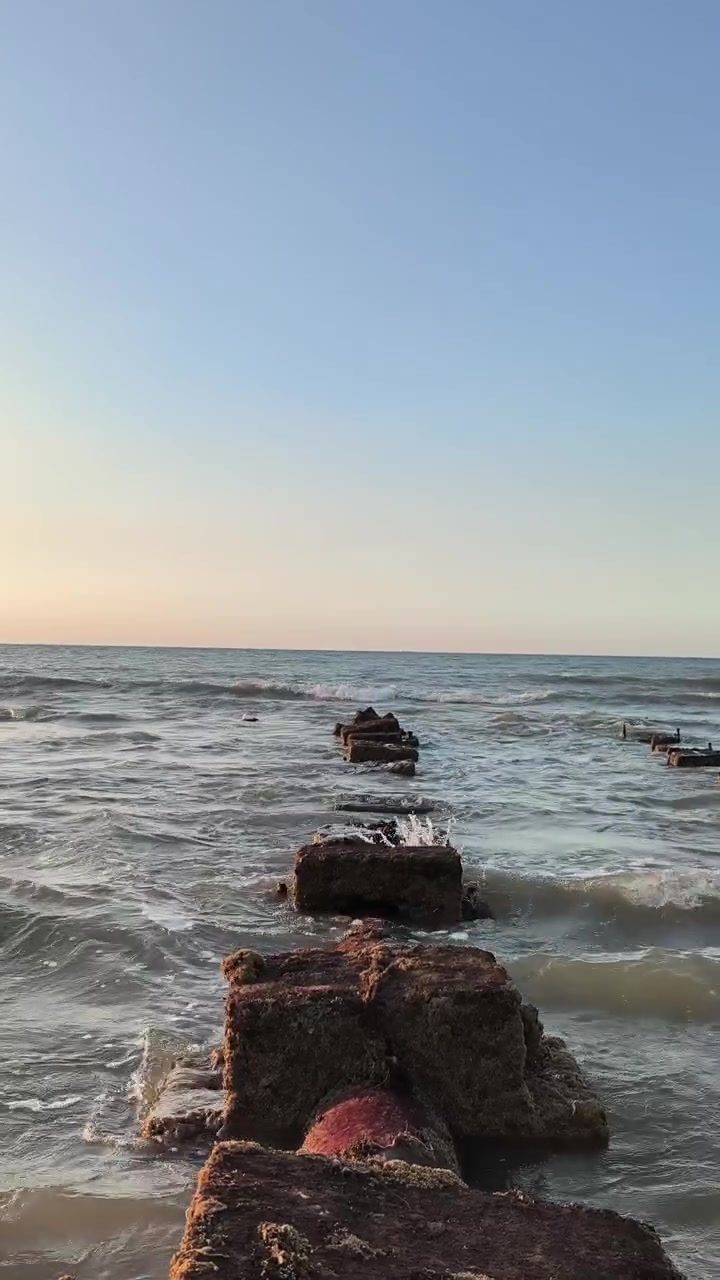 Ondas quebrando suavemente contra um antigo píer de pedra ao pôr do sol
