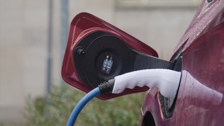 A closeup shot of the process of charging a red electric car with EV charger device on a rainy day in Jena city, Germany
