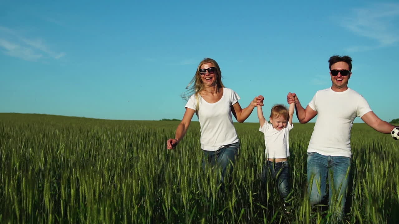 familia feliz: padre, madre e hijo, corriendo en el campo vestidos con camisetas blancas