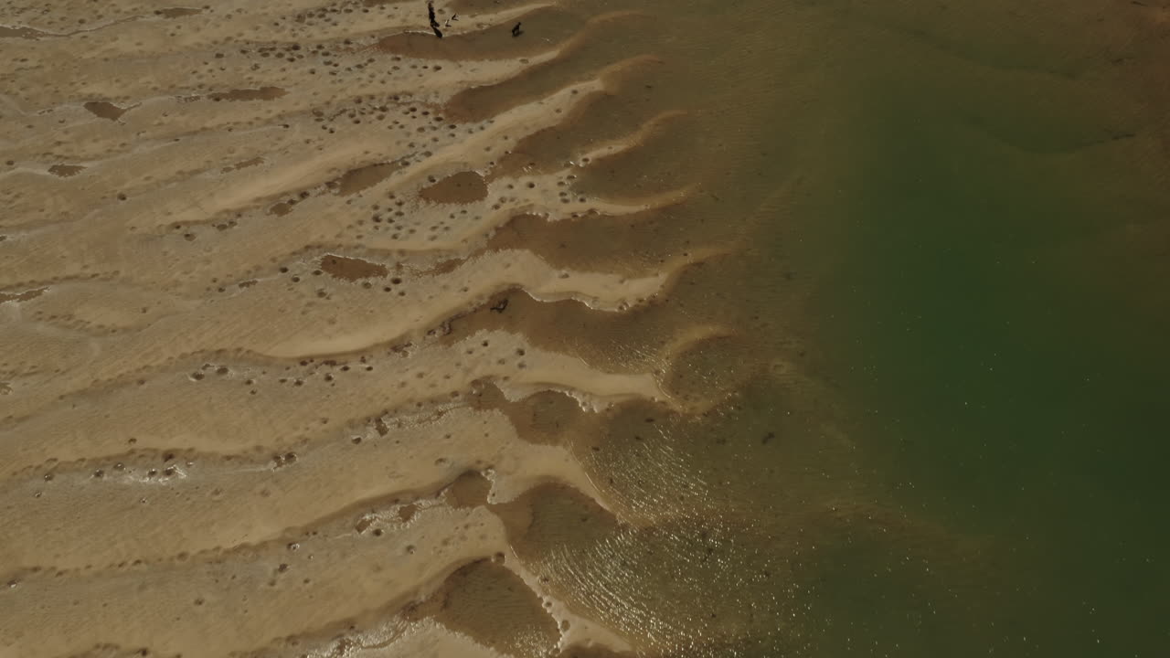 태양 아래 작은 개울 조명 옆에 있는 모래 패턴의 공중 하향식 샷 - 호주, 퀸즐랜드