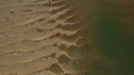 aerial top down shot of sandy pattern beside small stream lighting in sun - australia,queensland