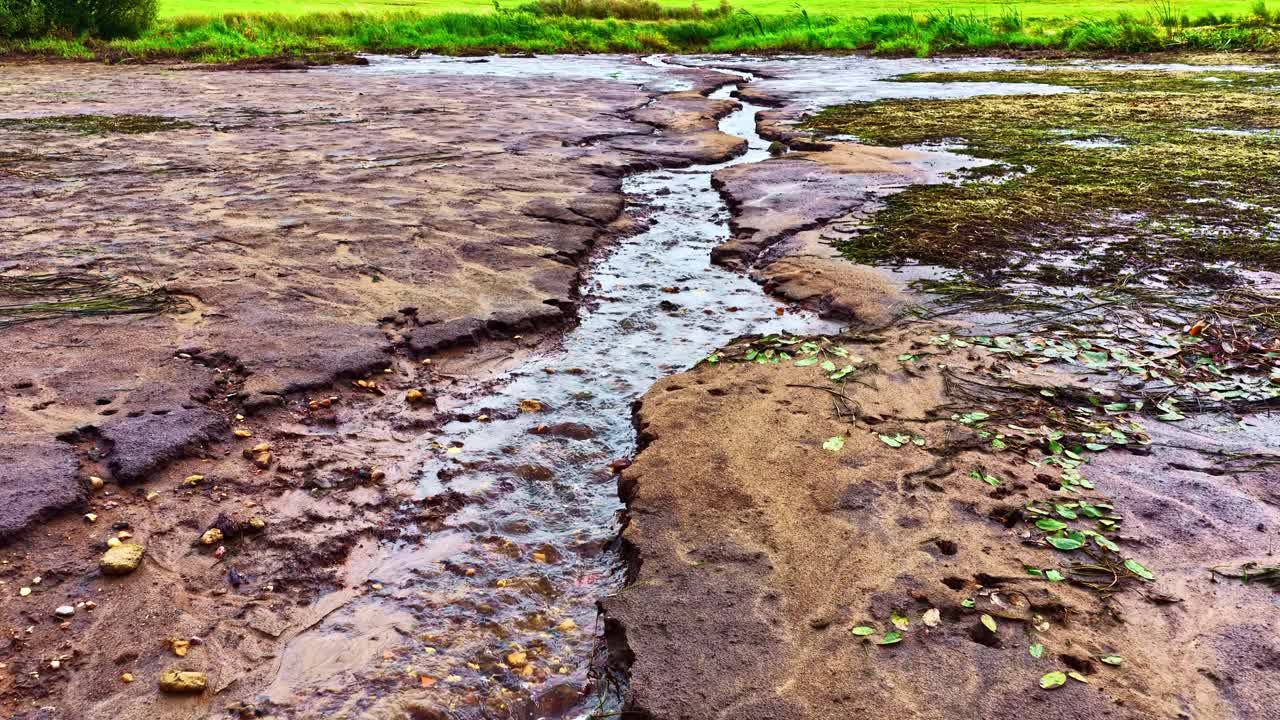 Shallow braided stream with muddy water and sediment deposits, upstream aerial above rocks and algae flats