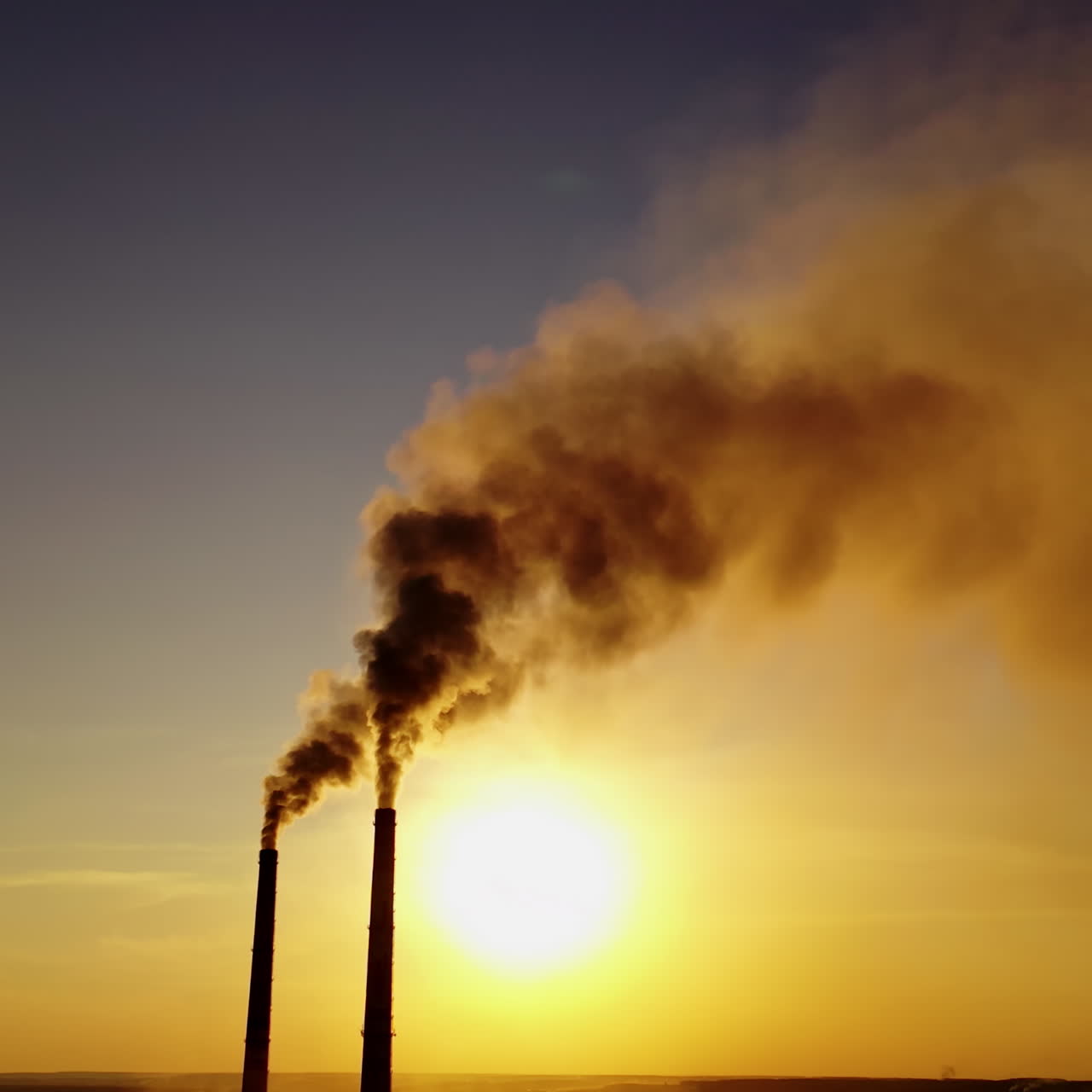 Dark smoke in the air. Two pipes from plant with chemical emissions in the sky at sunset. Ecological problems. Atmosphere in danger.